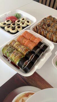 Assorted sushi rolls and Japanese food in plastic takeaway containers on a white table, close-up view of fresh colorful sushi selection for takeaway, delivery, restaurant and Asian cuisine