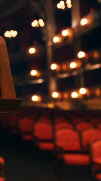 A view of an old theater shows red seats and glowing lights in the background. The empty rows suggest a quiet moment before the show starts.
