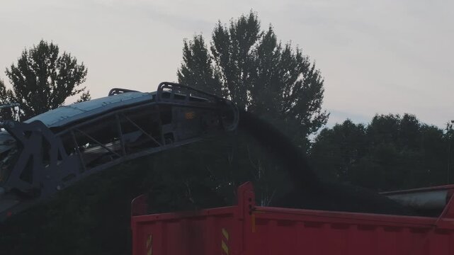 Heavy construction machinery working on road repairs. Cold planer loading milled asphalt from a pavement into a waiting dump truck