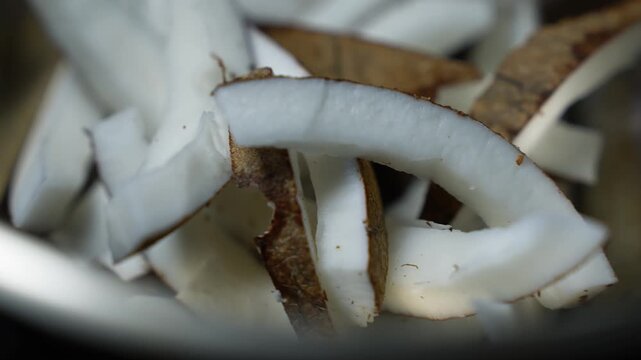 Close up of fresh coconut slices with white flesh and brown skin, showing a natural food texture