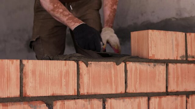 Mason applying mortar on ceramic brick wall during construction