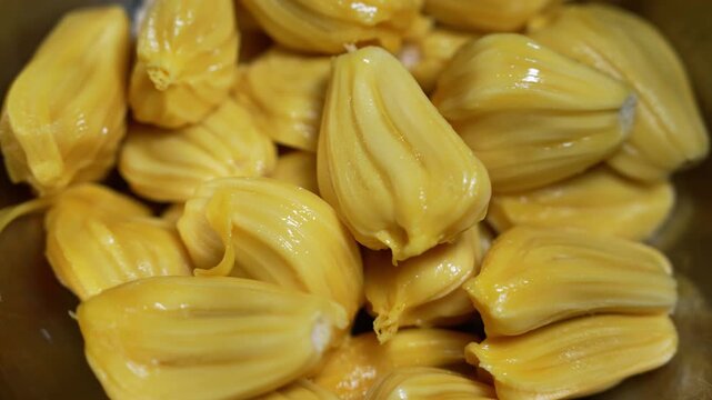 Close up of ripe jackfruit pods with glossy yellow flesh piled together, showing fresh tropical fruit texture and natural sweetness.
