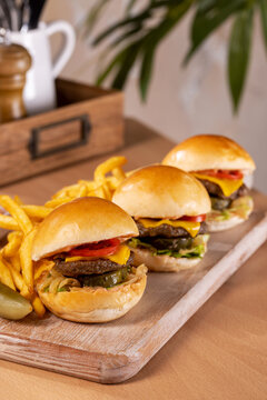 Trio of delicious mini beef sliders with melted cheese, tomato, and pickles, served with crispy french fries on a rustic wooden board.