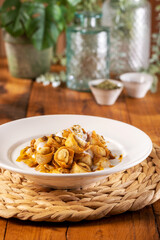 Fototapeta premium Traditional Turkish crispy fried manti (dumplings) topped with garlic yogurt and spiced chili butter sauce, served in a white bowl on a woven placemat over a warm wooden table.