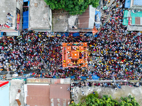 Savar, Bangladesh - 15 July 2024: Aerial view of the Rath Yatra festival, with a dense crowd surrounding a colorful chariot on a busy street, flanked by urban buildings and rooftops.
