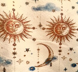 A vintage or tapestry-style fabric design featuring illustrated suns with faces, crescent moons, stars, and small blue clouds against a light cream background. © Anthony