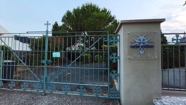Royan, France - July 15, 2026: Charente-Maritime. Nouvelle-Aquitaine. Green metal gate of Protestant cemetery with sign, trees and shrubs visible in background, peaceful setting
