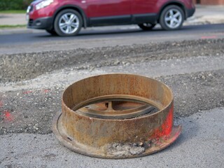 Raised rusty iron manhole cover on a milled asphalt road during resurfacing with passing traffic © light