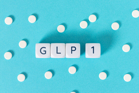 GLP 1 word on blocks surrounded by medicine pills on blue background