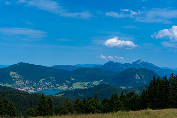 Fototapeta premium Scenic mountain landscape with forested hills, blue lake and valley settlement beneath a vivid summer sky with white clouds