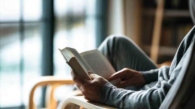 Peaceful lifestyle scene of a person reading a book in a comfortable chair near a large window, surrounded by warm modern interiors and soft natural daylight.
