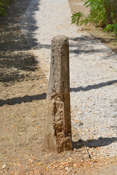 An old damaged concrete bollard stands at the edge of a light gravel path stretching into the distance