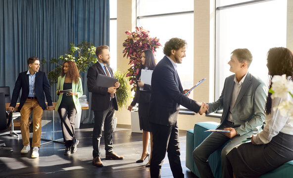 Business team meeting with handshake in office. Colleagues discuss partnership and agreement. Diverse professionals network by windows discussing strategy. Concept of teamwork and success.