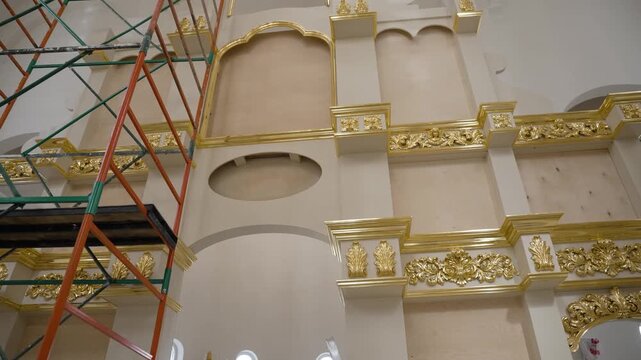 The new iconostasis in the new church during restoration work. A view of the interior with its ornate gold trim against the cream-colored walls during restoration. Gold leaf.
