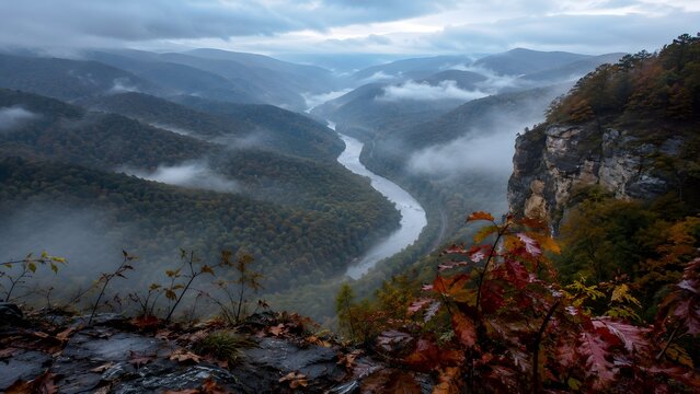 A winding river snakes through a misty, mountainous valley during a dramatic, overcast day, creating a scene of rugged, natural beauty and serene wilderness.