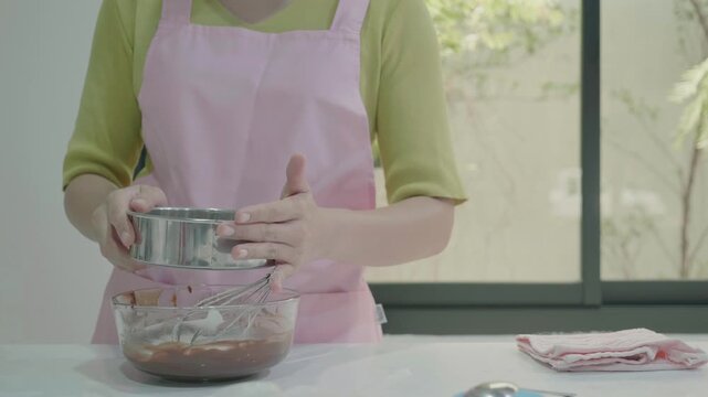 A person in a pink apron is preparing a mixture in a kitchen, holding a bowl and a whisk. The setting features a bright environment, emphasizing the joy of cooking and baking.