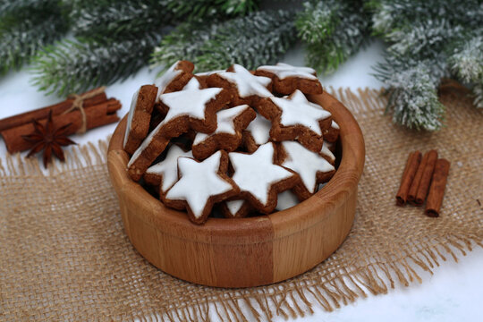 Holzschale mit  Zimtsternen  auf Jutedecke, daneben Zimtstangen und Tannenzweige.