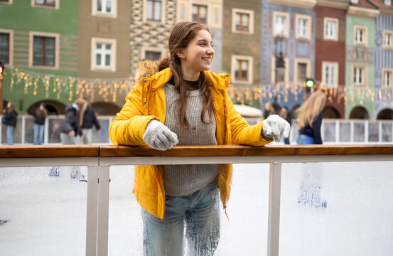Happy teenager rests on railing near ice rink in Poznan market square during cold winter daylight
