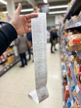 Person holding long paper receipt in supermarket aisle representing rising grocery prices inflation and high cost of living