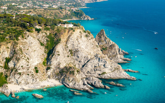 Capo Vaticano lighthouse 70mm telephoto view Calabria Italy. Dramatic vertical cliffs turquoise sea with anchored boats along scenic Tyrrhenian coast landscape. High resolution print.