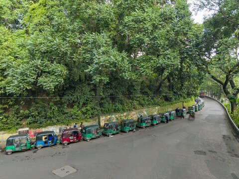 Chittagong, Bangladesh - 03 August 2026: Aerial view of a line of green auto-rickshaws parked along a road near the lush hillside of CRB Chittagong.