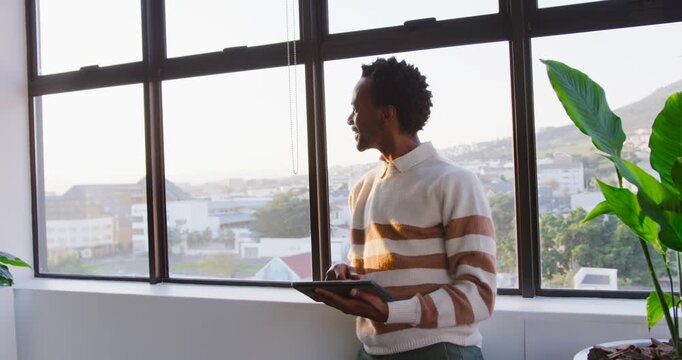African American man in striped sweater at window scanning view, then tapping tablet checking email