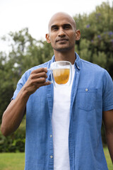 Adult African American man holding double-walled glass mug of tea standing in yard in denim shirt © wavebreak3