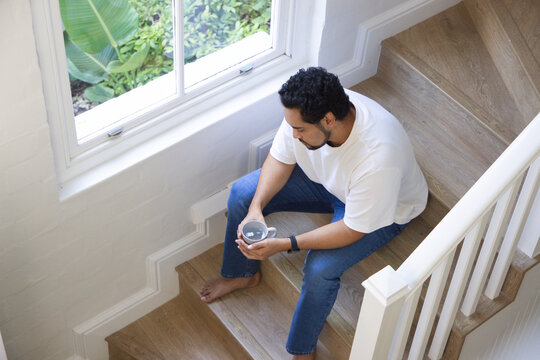 African American man sitting on wooden stairs holding round device, wearing smartwatch