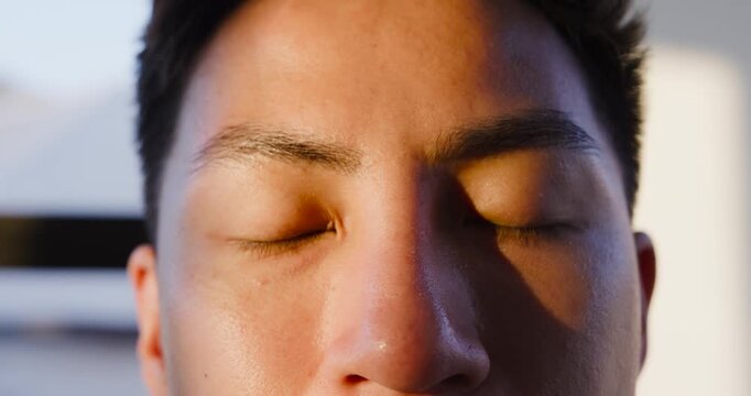Mid Adult Asian male reacting to warm sunlight, slowly opening eyes toward camera and blind