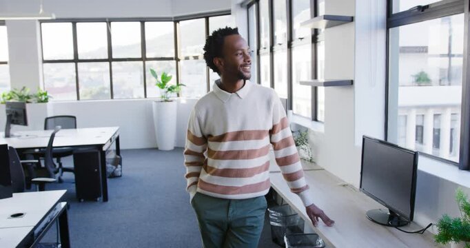 African American man standing at sill starting looking out window in office turning and smiling