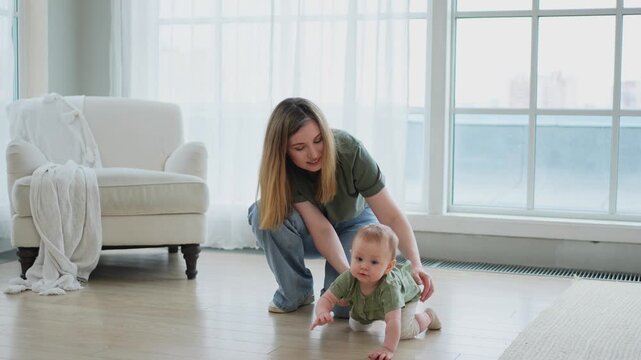 Baby development. First steps. Little infant girl making first steps at home. Happy mother supporting baby first steps. Mom helping toddler child walking in living room. Happy family at home