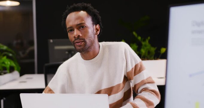 African American man checking laptop at desk leaning reaching tablet showing screen explaining
