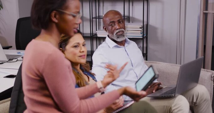 Diverse team starting meeting in office, presenter tapping tablet, peers using laptop, copy space