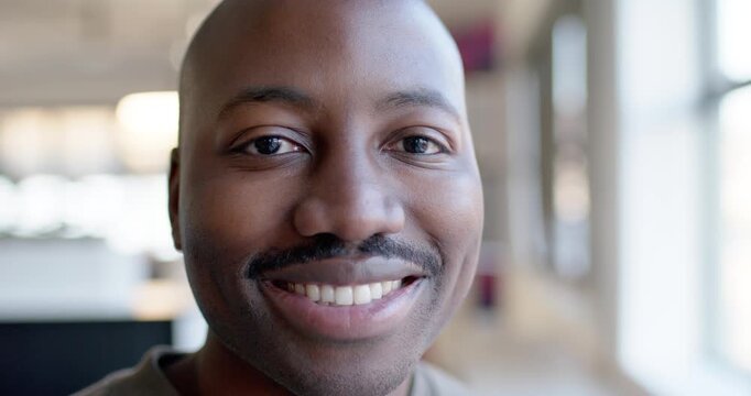 Adult man facing camera, smiling then laughing during camera recording in office with large windows