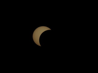 A partial solar eclipse appears as a bright golden crescent against a pitch-black sky over Mioglia, Italy. © Roberto