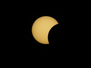 A partial solar eclipse over Mioglia, Italy, showing a yellow crescent sun against a dark sky. © Roberto