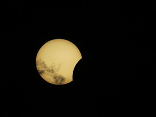 A partial solar eclipse is visible in the dark sky above Mioglia, Italy, with thin clouds drifting across the glowing sun. © Roberto