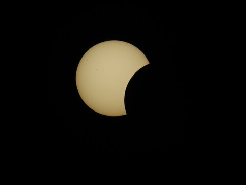 A summer evening partial solar eclipse over Mioglia, Italy, with the Sun partially obscured by the Moon against a dark sky.