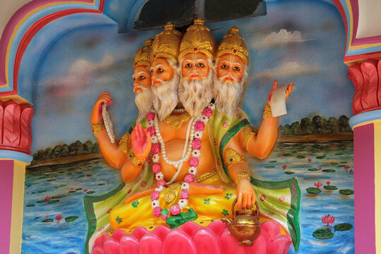 Colorful statue of four-headed Hindu god Lord Brahma sitting on a lotus inside a temple niche.