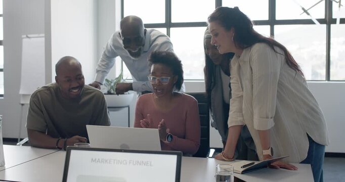 Diverse team in business attire cheering around woman operating laptop at table after funnel win