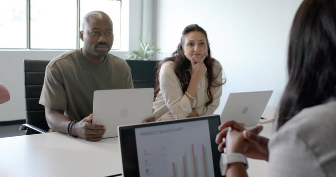 Diverse team speaking while presenter adjusting watch and showing laptop chart at conference table