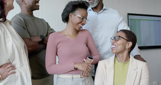 Diverse coworkers responding to charts on monitor, smiling, leaning, posing by meeting chair