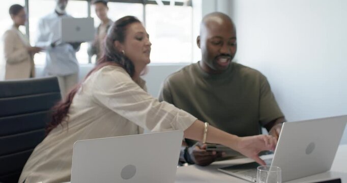 Diverse team meeting at table with monitor showing sales chart initiating woman explaining gestures