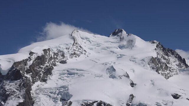 View of the snow-covered Gornergrat mountain peak with jagged rocky ridges and glaciers under a clear blue sky in Zermatt, Valais, Switzerland.