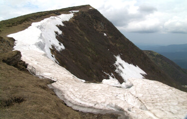 Large cornice of snow clinging to a steep mountain peak ridge in spring © baxys