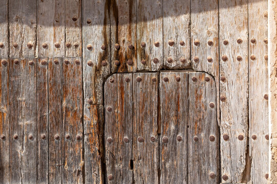 Old and time-worn solid wooden door with decorative metal elements
