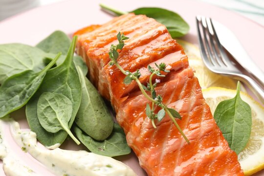 Piece of grilled salmon with thyme, basil, lemon and sauce on table, closeup