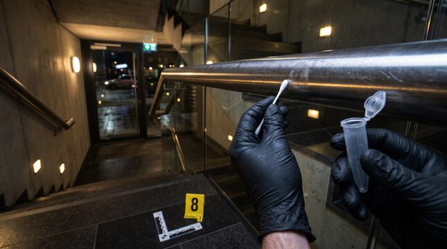 Forensic investigator collecting trace evidence with a swab from a stairway handrail at a crime scene, documenting evidence for criminal investigation and forensic analysis