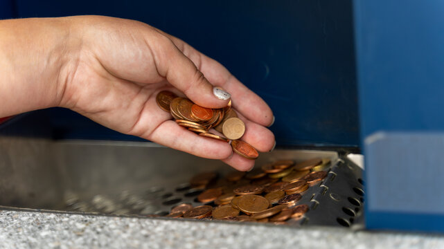 Hand Holding Coins Over a Coin Sorting Machine