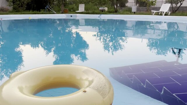 Round blue swimming pool with yellow float and tree reflections
